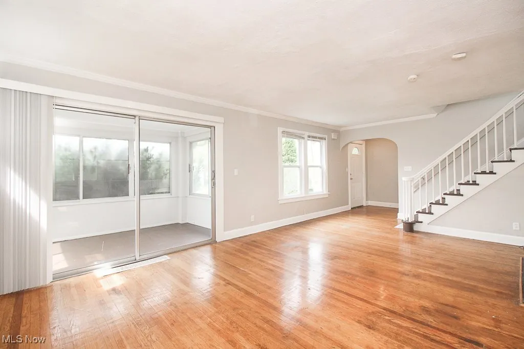 Unfurnished living room featuring arched walkways, stairway, light wood finished floors, and crown molding