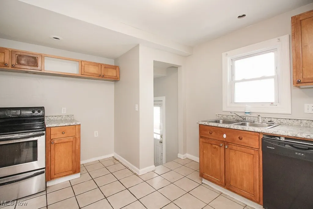Kitchen with dishwasher, stainless steel electric stove, light countertops, light tile patterned floors, and brown cabinets