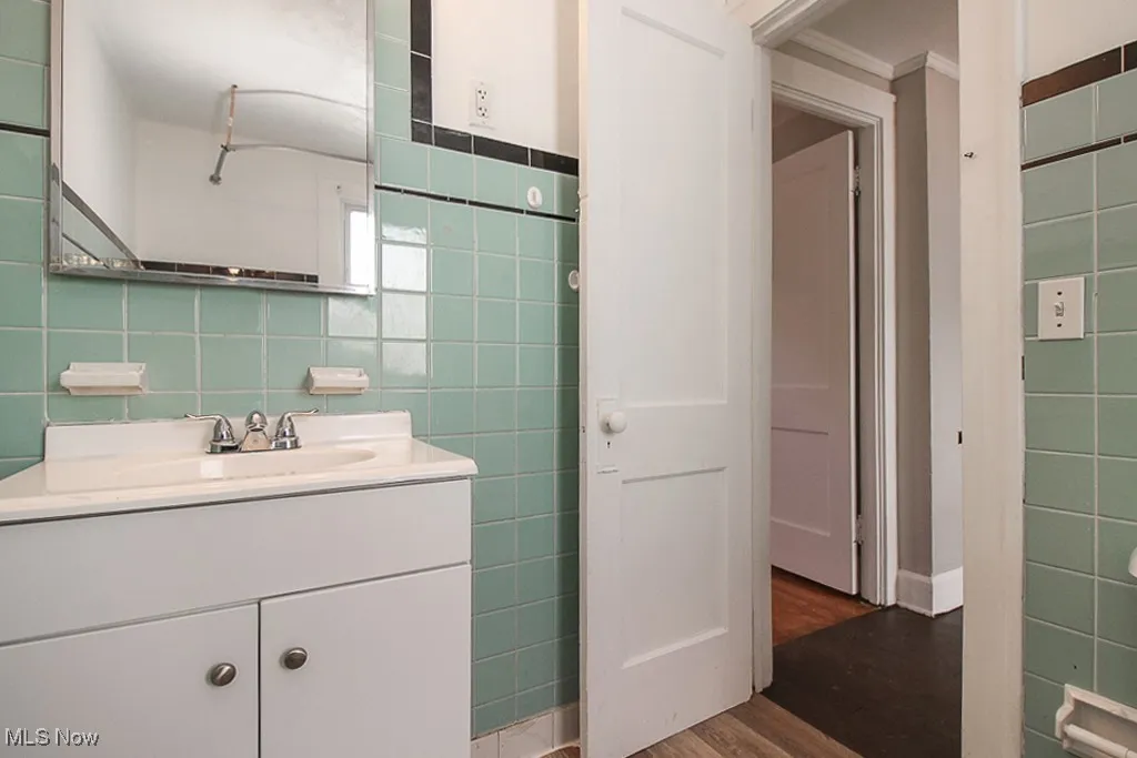 Bathroom with tile walls, wood finished floors, vanity, and crown molding