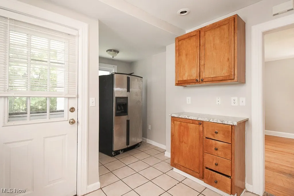 Kitchen with stainless steel fridge, brown cabinets, light tile patterned floors, and light stone counters