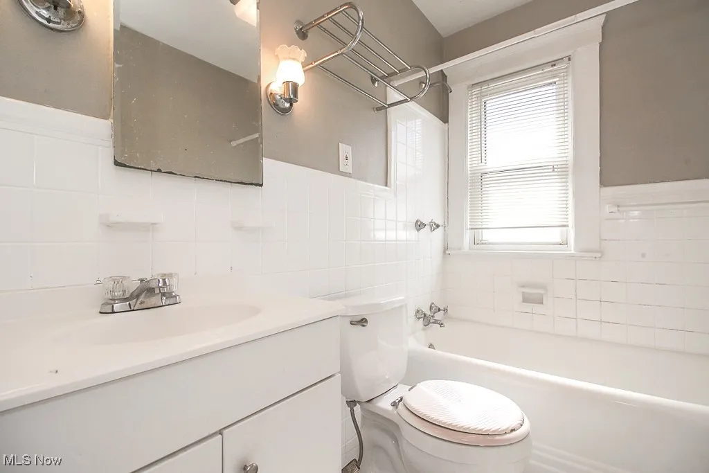 Bathroom with tile walls, a tub to relax in, vanity, and a wainscoted wall