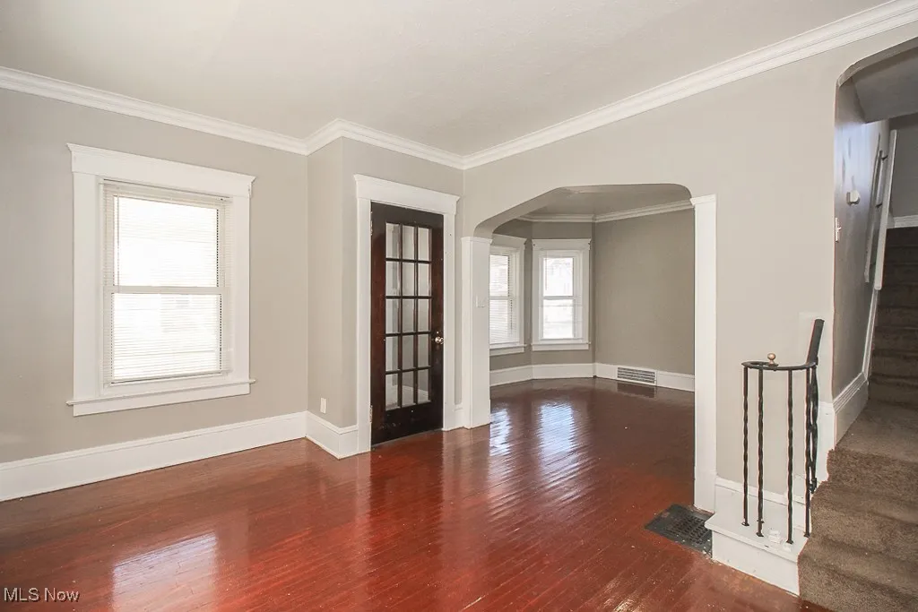 Empty room with arched walkways, wood finished floors, stairway, and ornamental molding