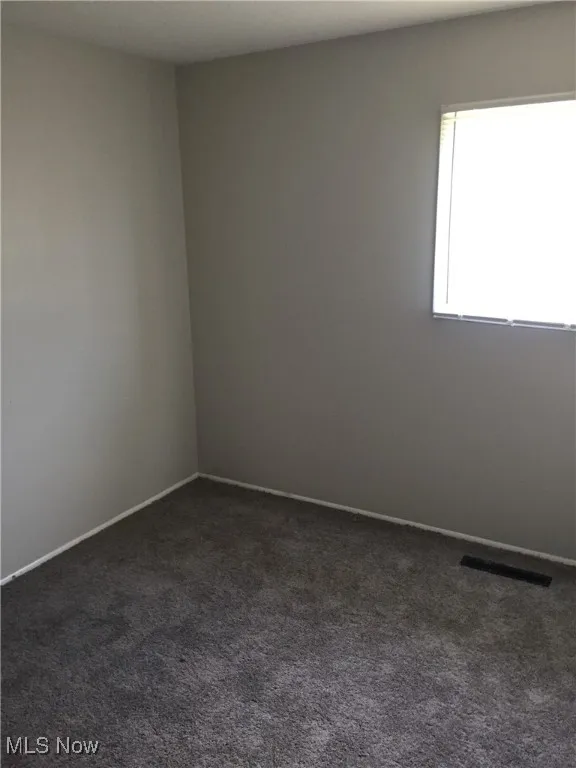 Unfurnished room featuring dark colored carpet and baseboards