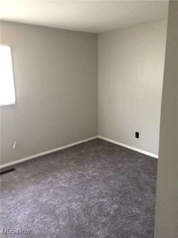 Spare room with dark colored carpet and baseboards