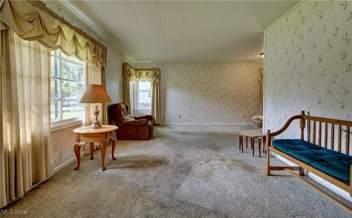 Living area featuring wallpapered walls, carpet, and ornamental molding