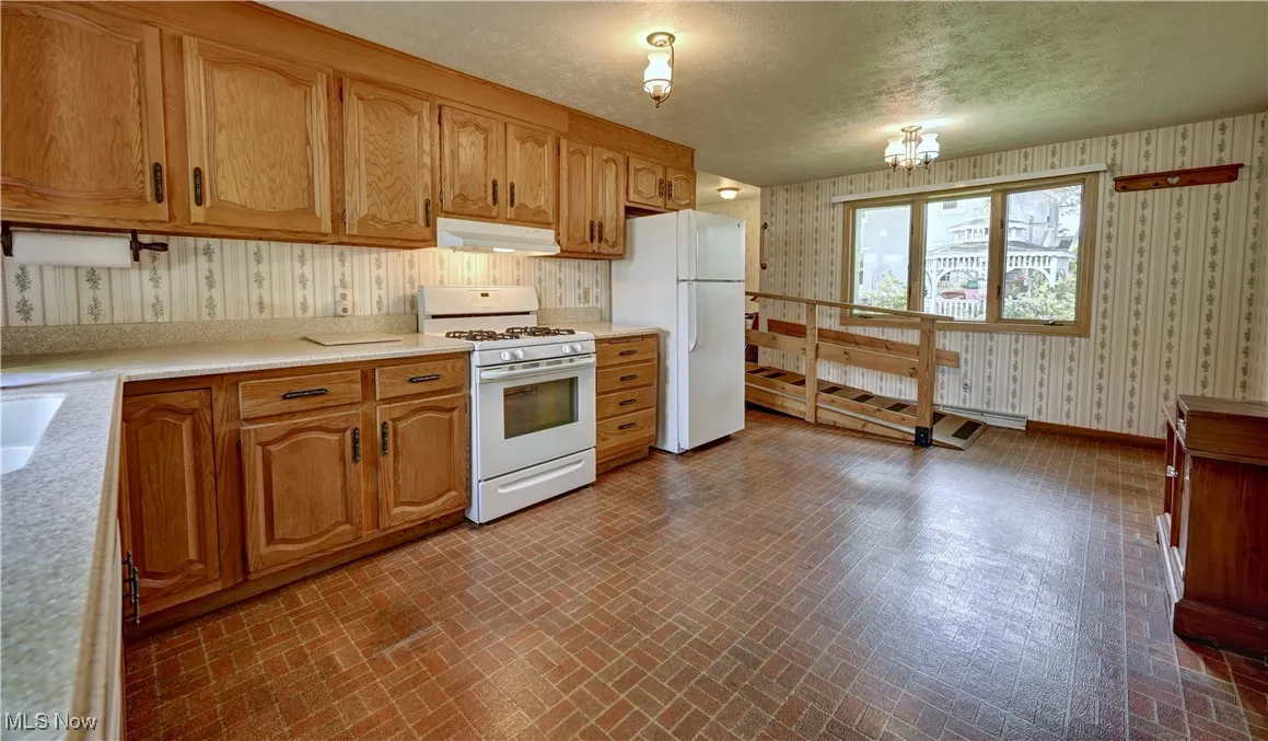 Kitchen with white appliances, wallpapered walls, brick patterned flooring, under cabinet range hood, and light countertops