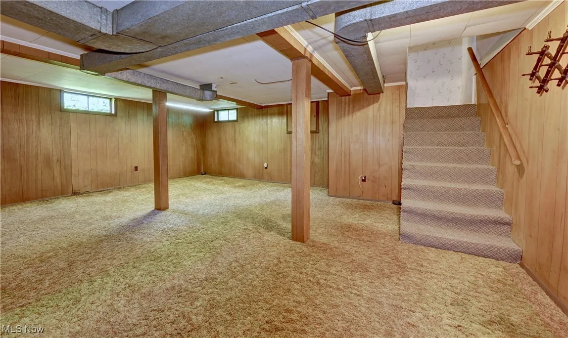 Basement featuring carpet flooring, stairs, and wood walls