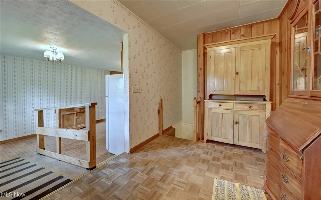 Kitchen with wallpapered walls, glass insert cabinets, a chandelier, and light brown cabinetry
