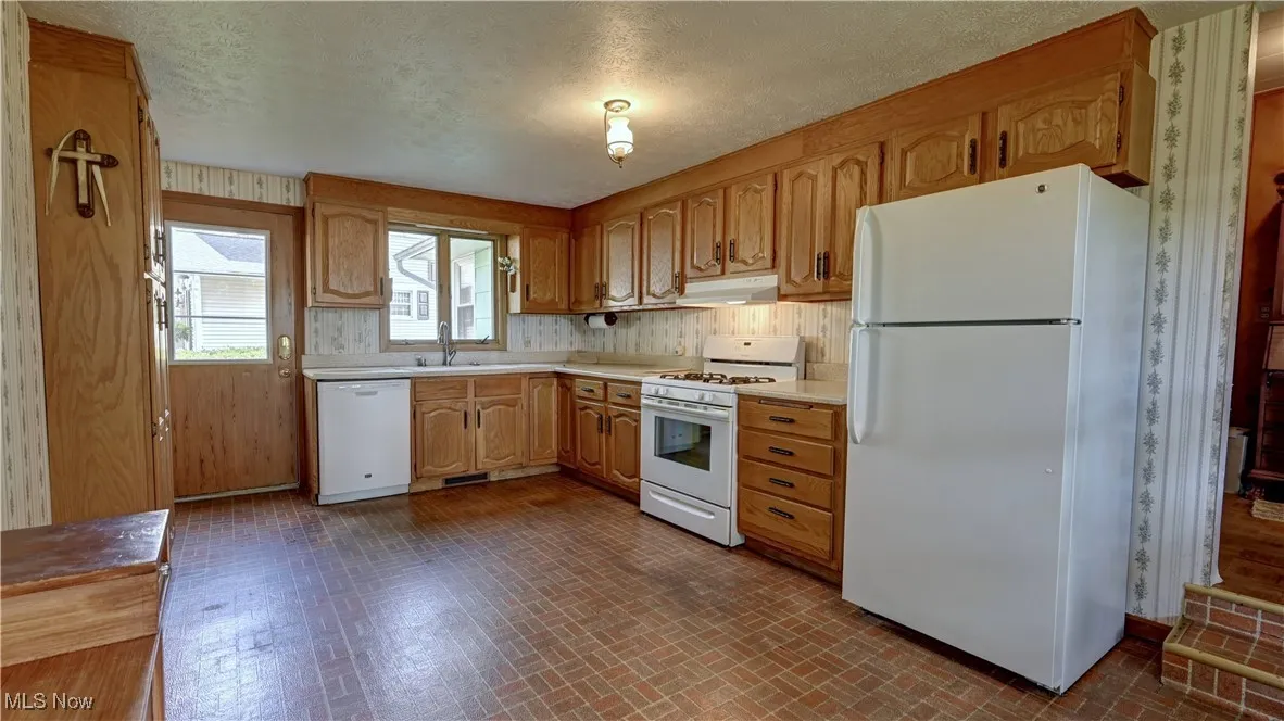 Kitchen featuring white appliances, under cabinet range hood, light countertops, brick patterned floors, and a textured ceiling
