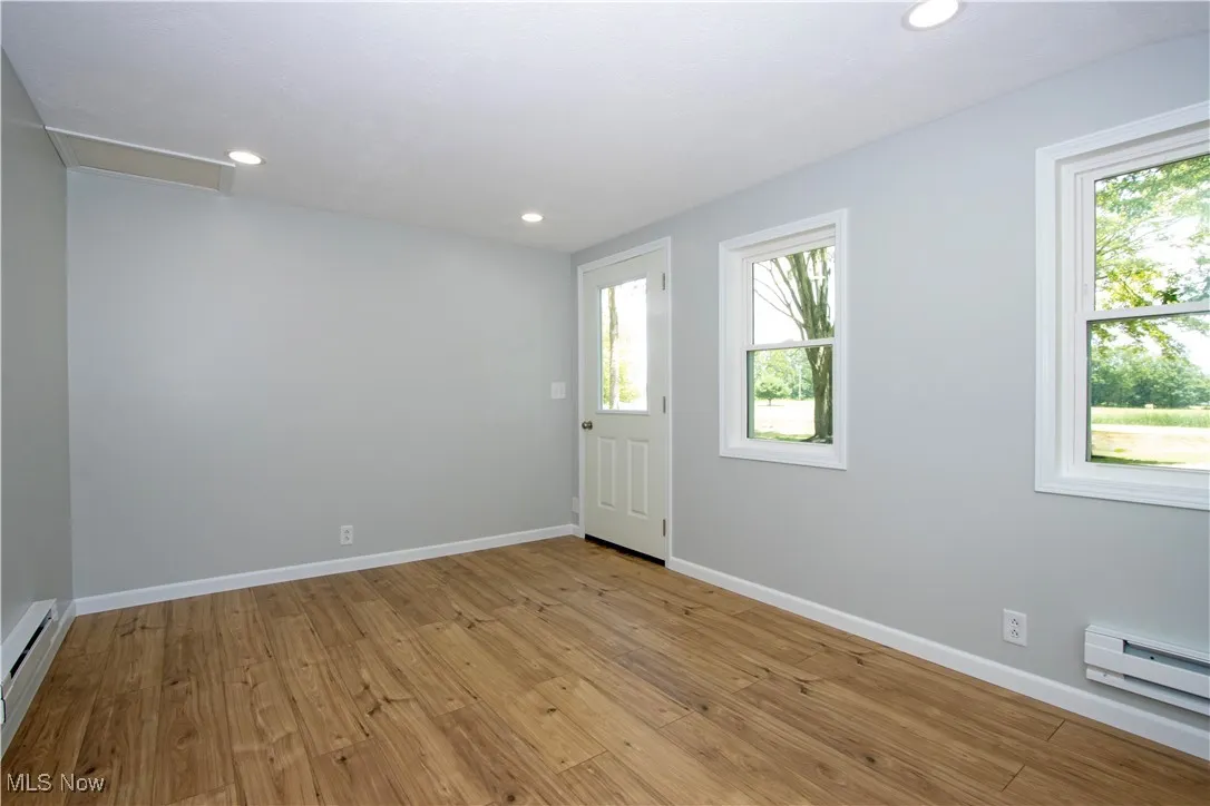 Spare room with a baseboard heating unit, light wood-type flooring, recessed lighting, and attic access