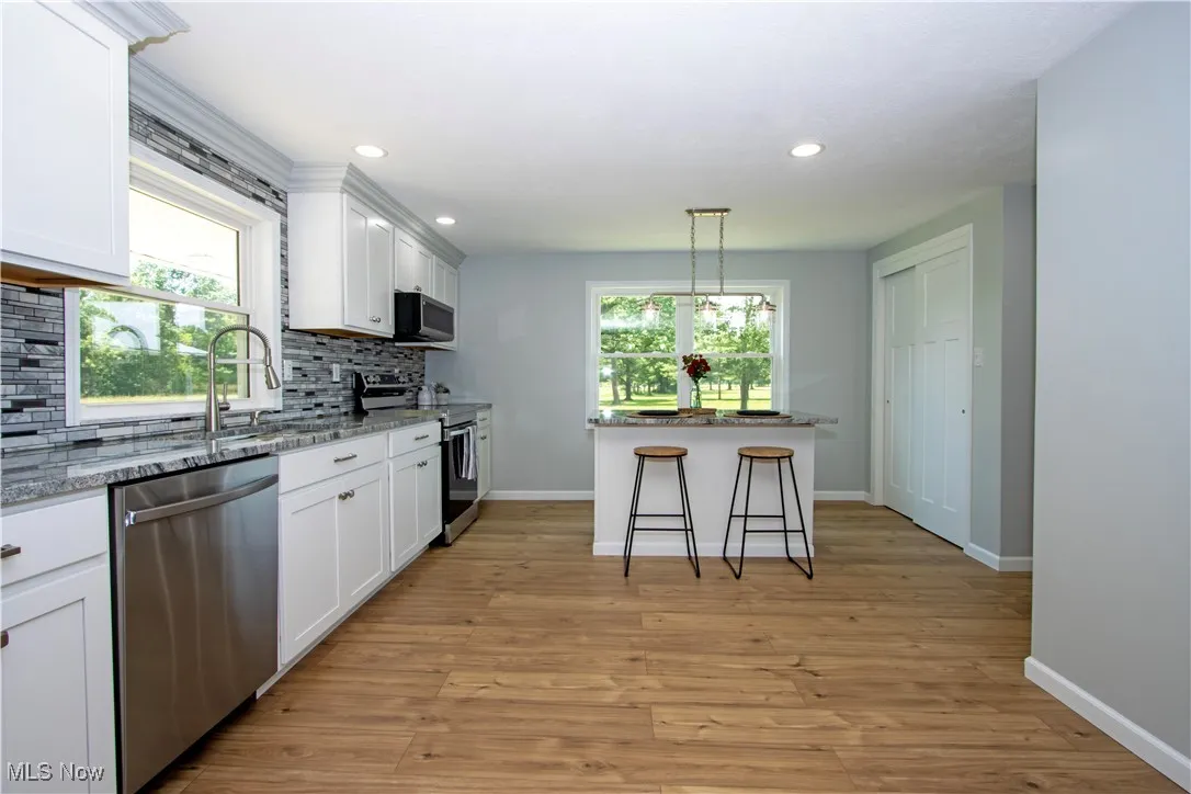 Kitchen with appliances with stainless steel finishes, decorative backsplash, white cabinets, light stone counters, and recessed lighting