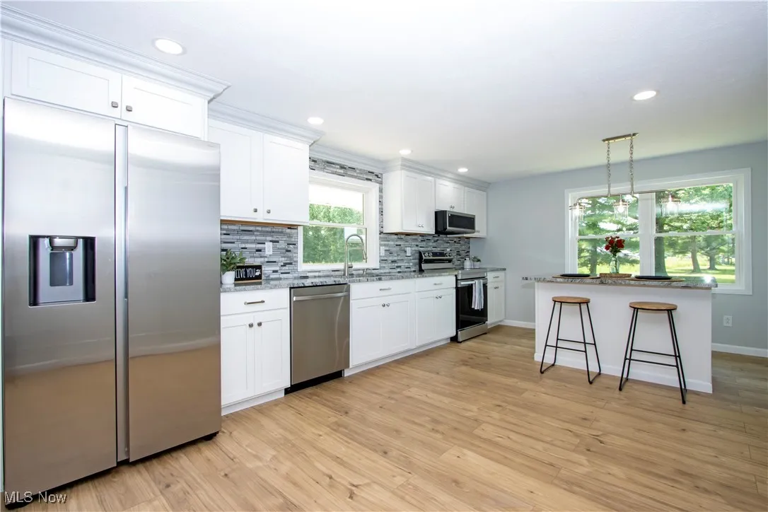Kitchen featuring stainless steel appliances, backsplash, white cabinets, light wood-type flooring, and a breakfast bar