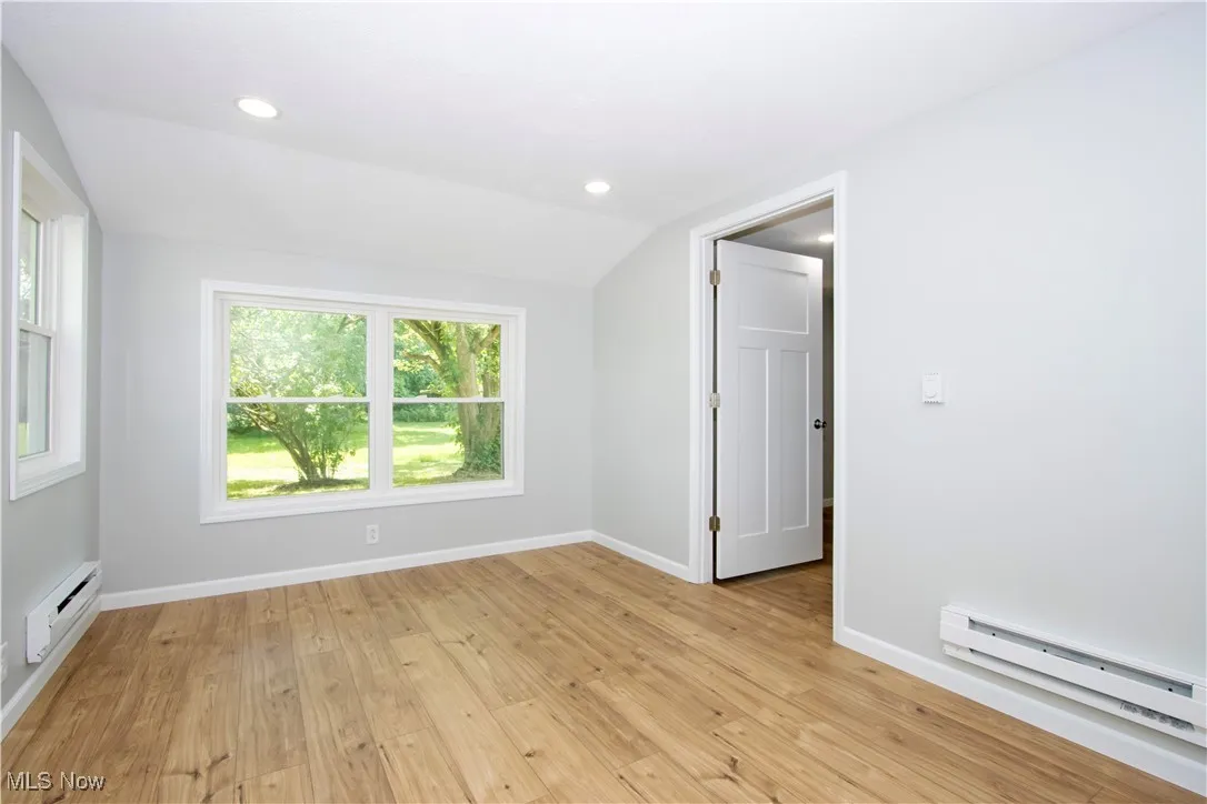 Empty room featuring a baseboard radiator, vaulted ceiling, light wood finished floors, and recessed lighting