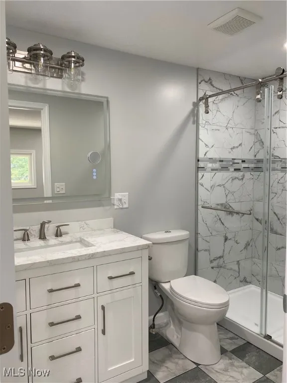 Full bath featuring a marble finish shower, vanity, and marble look tile flooring
