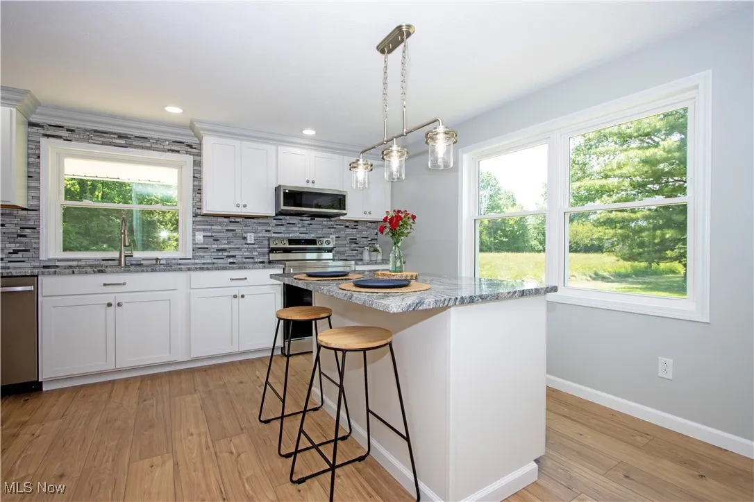Kitchen with stainless steel appliances, backsplash, light wood-style floors, white cabinets, and recessed lighting
