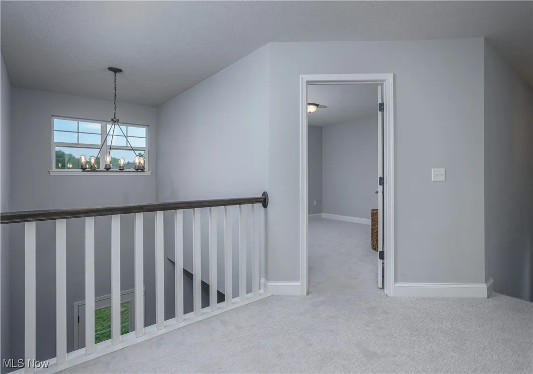 Hallway with carpet flooring, a chandelier, and an upstairs landing