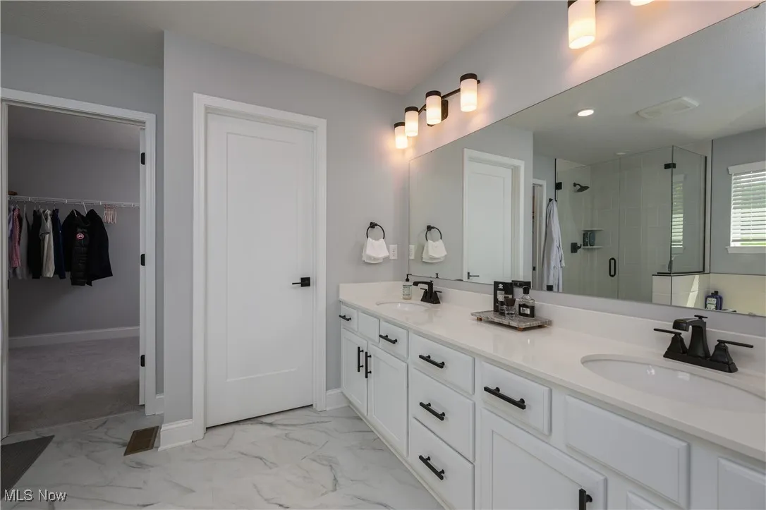 Full bathroom with a shower stall, double vanity, marble finish floors, and a spacious closet