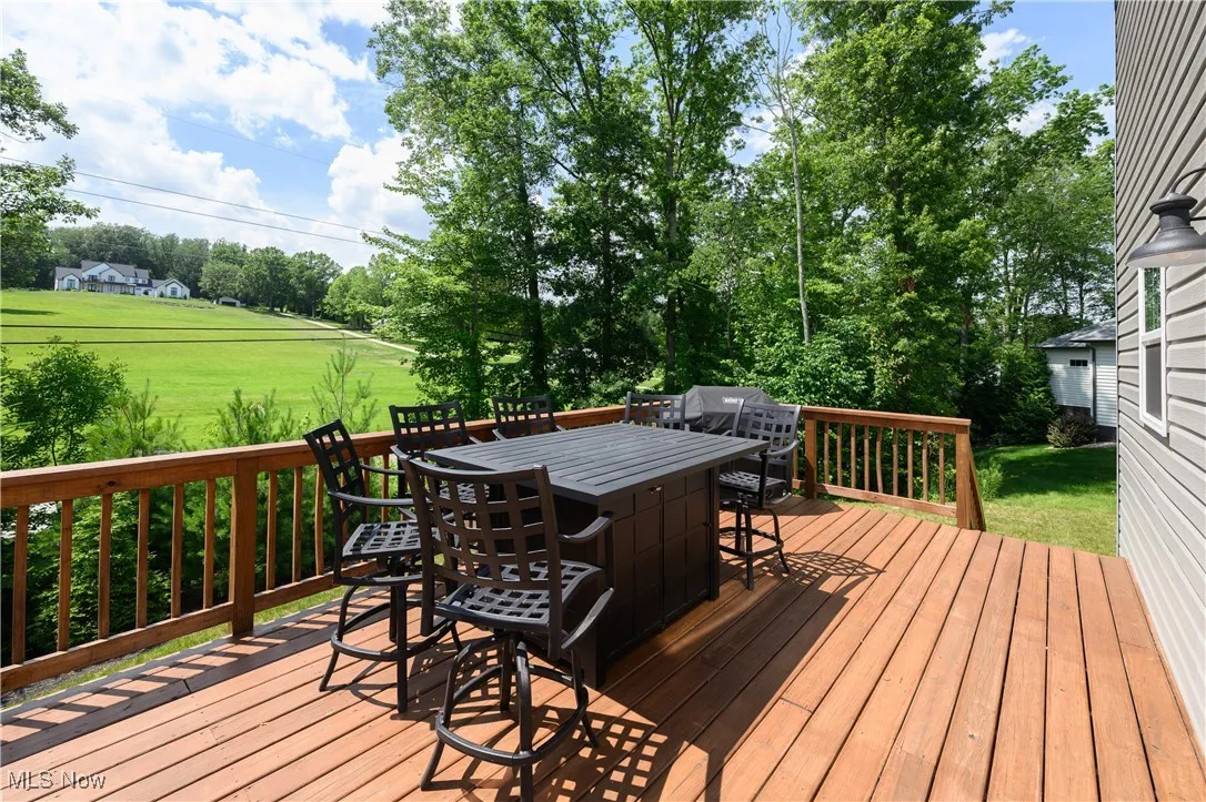 Deck featuring view of scattered trees, a yard, and outdoor dining area