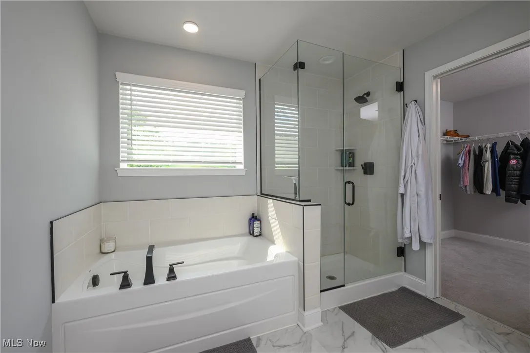 Full bath featuring a garden tub, a stall shower, a spacious closet, and marble look tiles