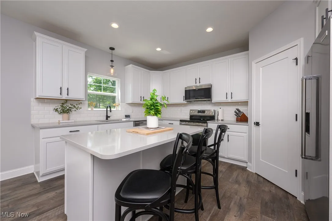Kitchen with stainless steel appliances, dark wood-style flooring, white cabinets, light countertops, and a center island