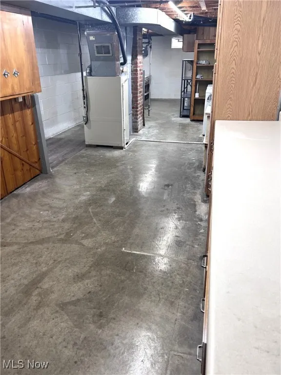 Unfinished below grade area with heating unit and concrete block wall