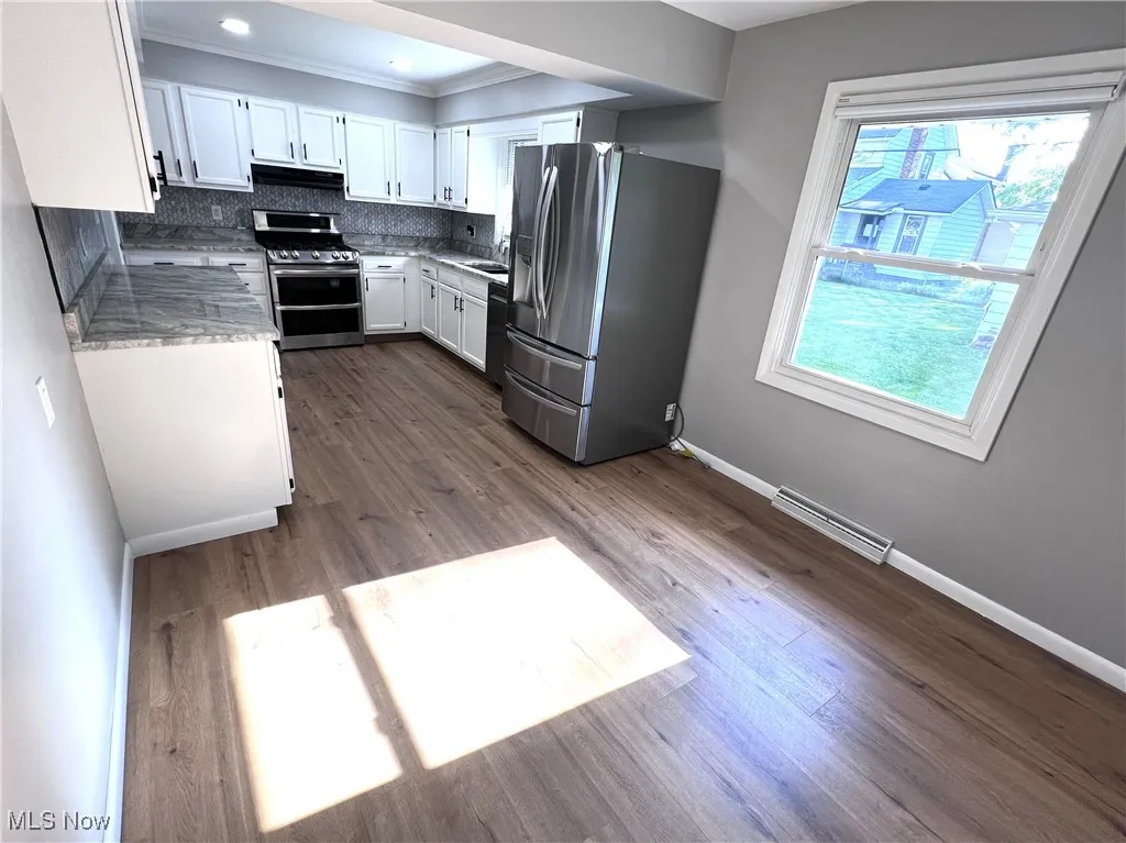 Kitchen with appliances with stainless steel finishes, white cabinetry, decorative backsplash, dark wood finished floors, and ornamental molding