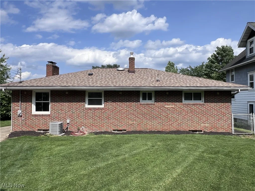 Rear view of property with a chimney, brick siding, a lawn, and roof with shingles
