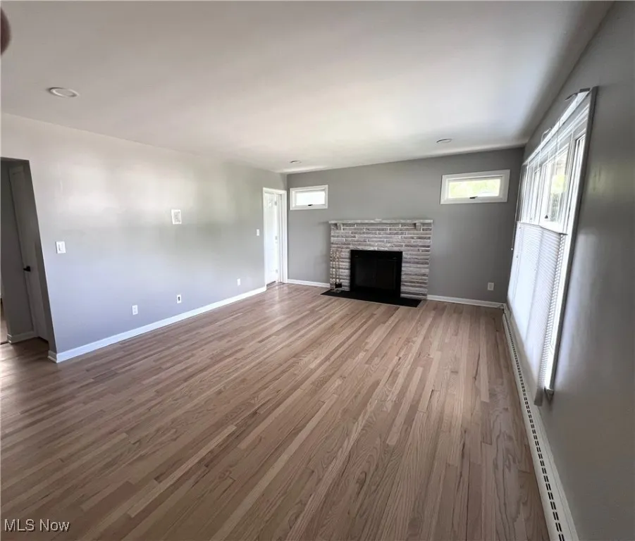 Unfurnished living room with wood finished floors, a fireplace, and a baseboard heating unit