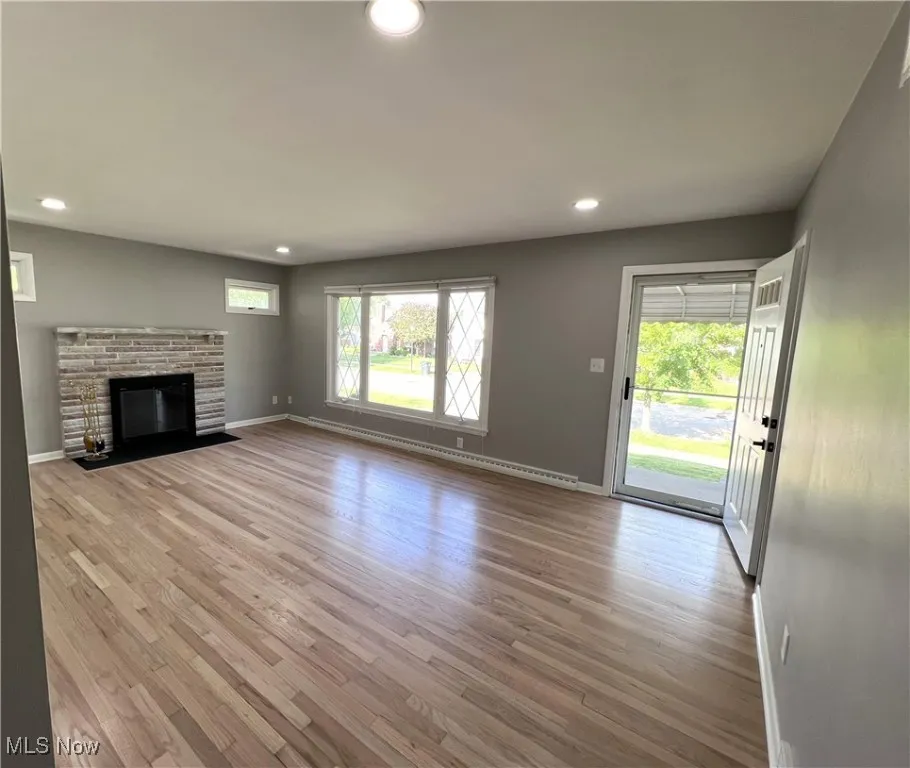 Unfurnished living room with recessed lighting, plenty of natural light, wood finished floors, a brick fireplace, and baseboard heating