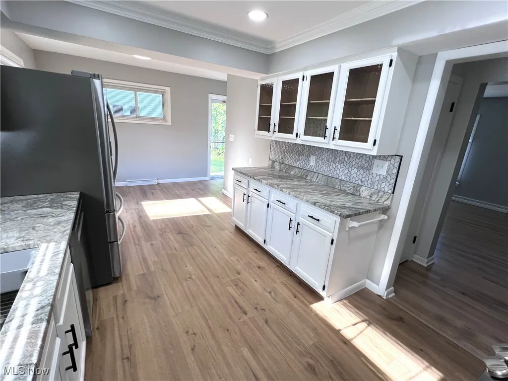 Kitchen featuring freestanding refrigerator, crown molding, white cabinetry, light stone countertops, and glass insert cabinets