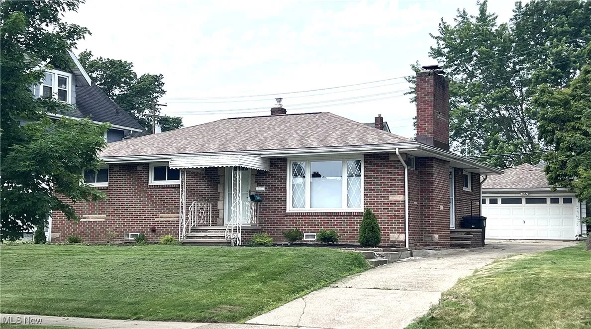 View of front facade with a chimney, brick siding, a front yard, and roof with shingles