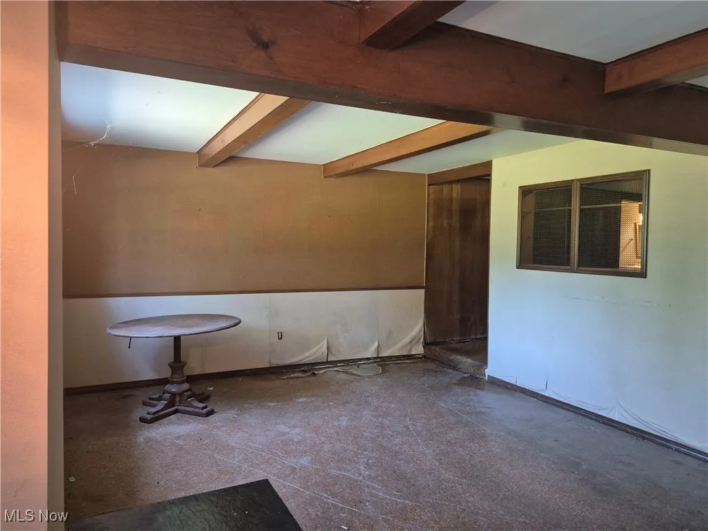 Unfurnished room with beamed ceiling and concrete floors