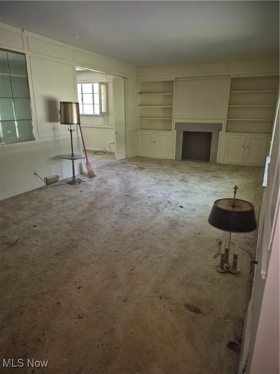 Unfurnished living room with carpet and built in shelves