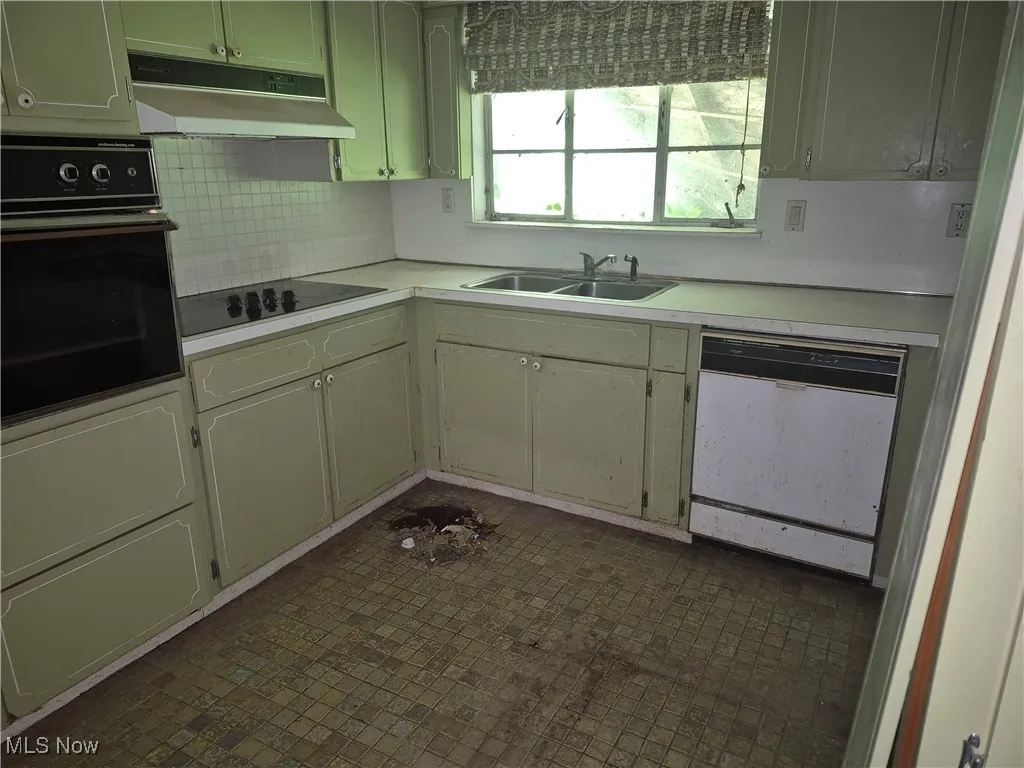 Kitchen featuring black appliances, under cabinet range hood, light countertops, and tasteful backsplash