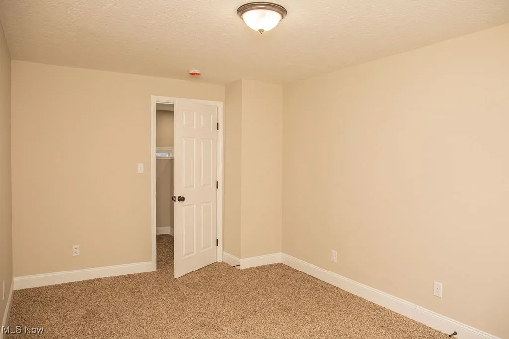 Empty room with light colored carpet, a textured ceiling, and a smoke detector
