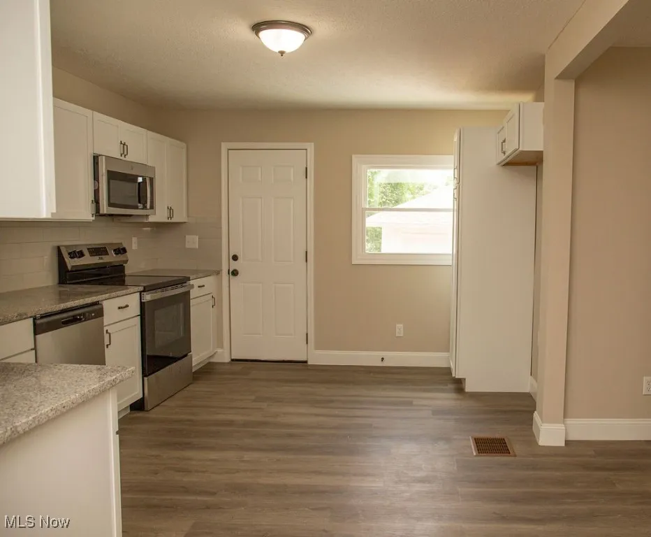 Kitchen with stainless steel appliances, white cabinetry, tasteful backsplash, dark wood-style floors, and a textured ceiling