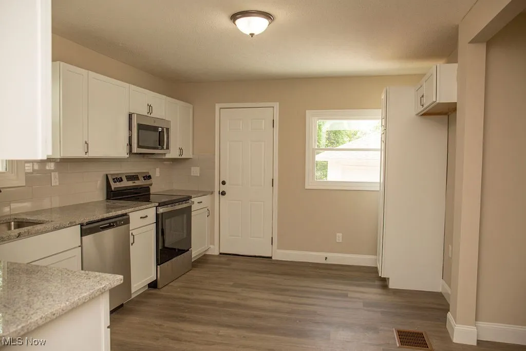 Kitchen with appliances with stainless steel finishes, white cabinets, tasteful backsplash, wood finished floors, and light stone countertops