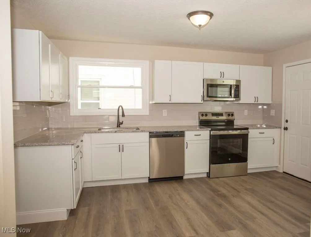 Kitchen with appliances with stainless steel finishes, dark wood finished floors, white cabinetry, tasteful backsplash, and a textured ceiling