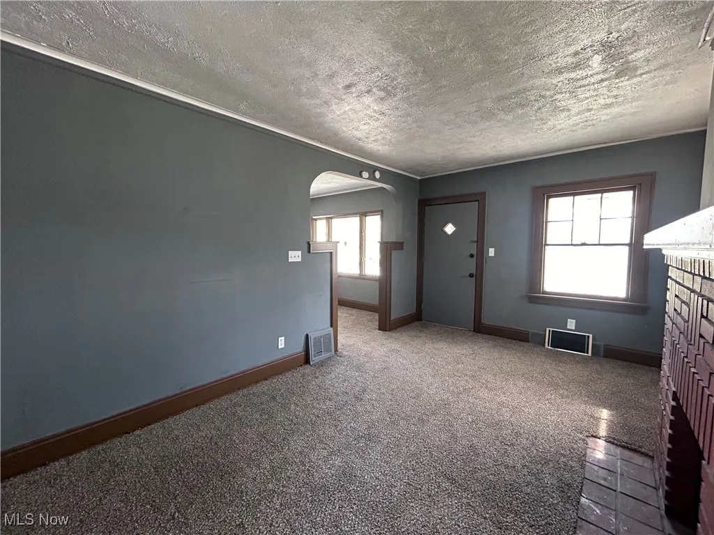 Unfurnished living room with a textured ceiling, arched walkways, a fireplace, and carpet floors