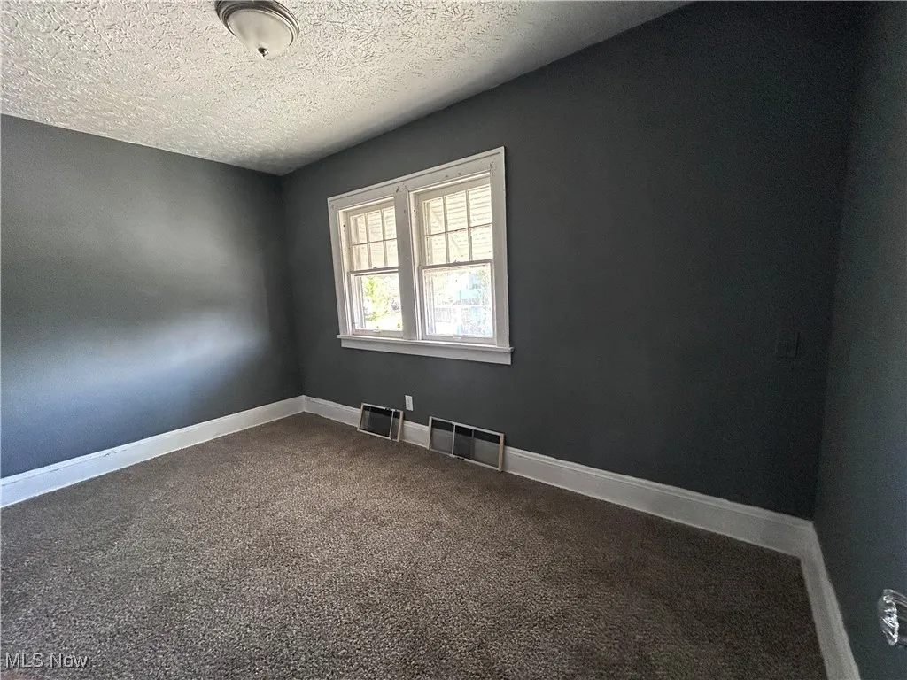 Spare room with a textured ceiling and dark colored carpet