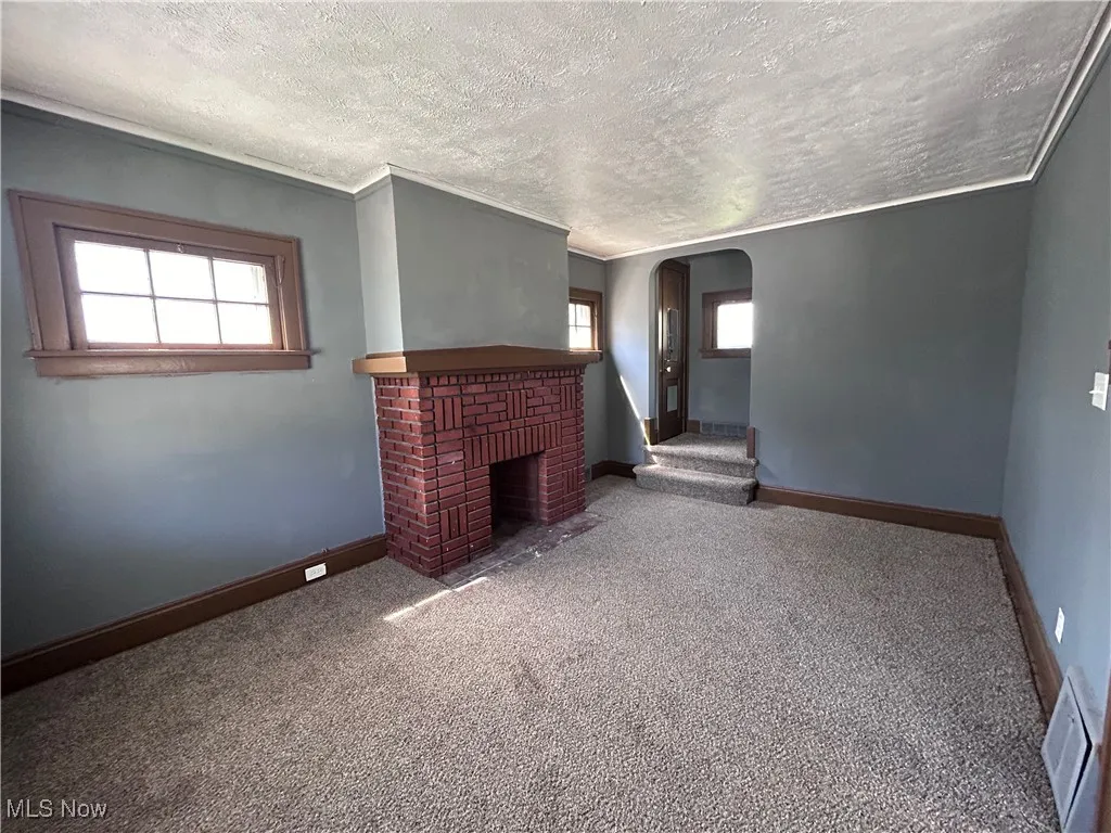 Unfurnished living room with arched walkways, carpet, a textured ceiling, and a fireplace