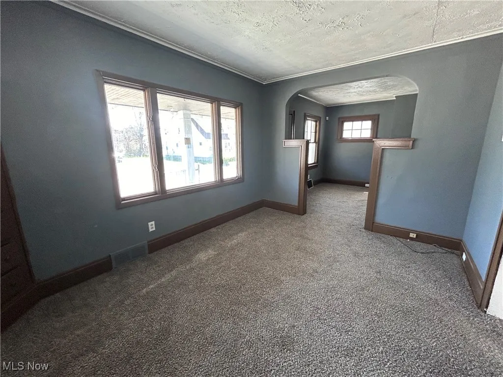 Carpeted spare room with arched walkways, crown molding, and a textured ceiling