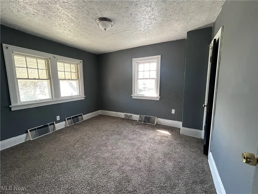 Carpeted spare room with a textured ceiling and a baseboard radiator