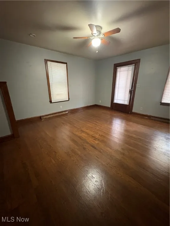 Unfurnished room with dark wood-type flooring, ceiling fan, and a baseboard heating unit