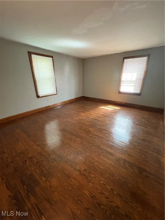 Unfurnished room with a textured wall and dark wood-style floors