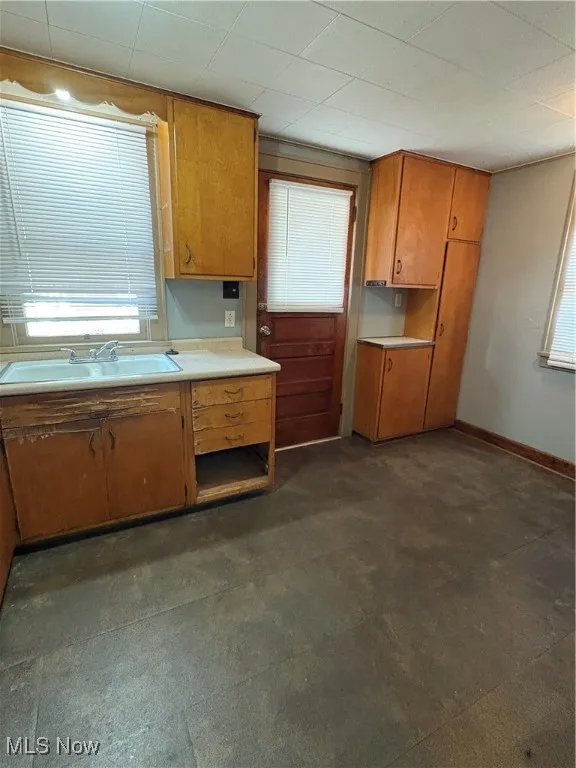 Kitchen featuring light countertops, brown cabinetry, dark flooring, and healthy amount of natural light