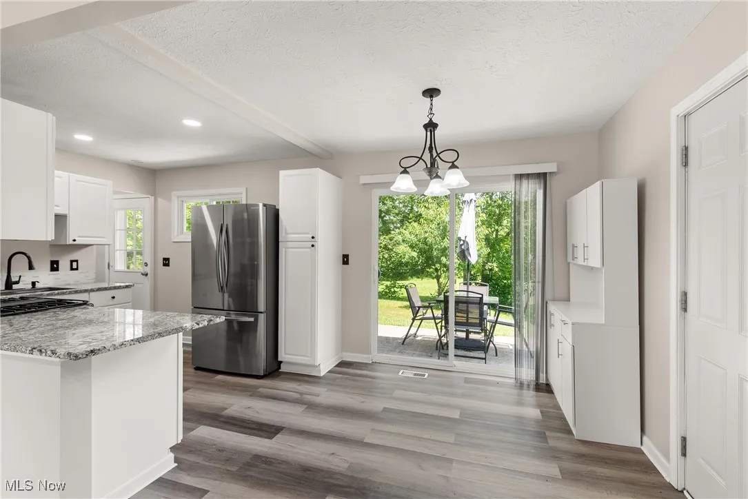 Kitchen featuring freestanding refrigerator, white cabinets, light stone countertops, recessed lighting, and a textured ceiling