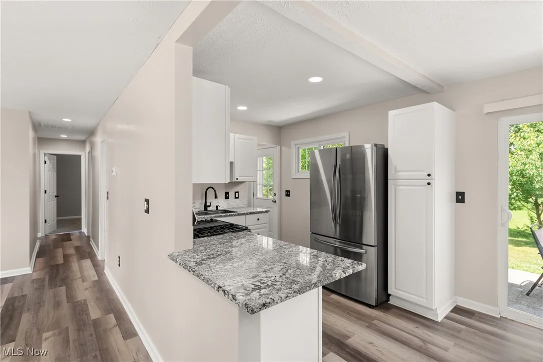 Kitchen with freestanding refrigerator, light stone counters, light wood finished floors, white cabinets, and recessed lighting