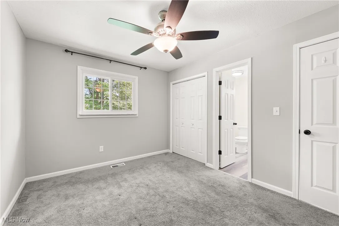 Unfurnished bedroom with carpet, a closet, ensuite bathroom, and a ceiling fan