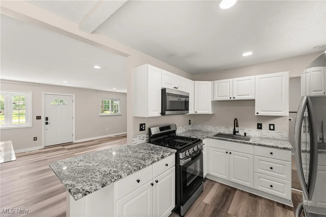 Kitchen featuring appliances with stainless steel finishes, wood finished floors, light stone countertops, white cabinetry, and recessed lighting